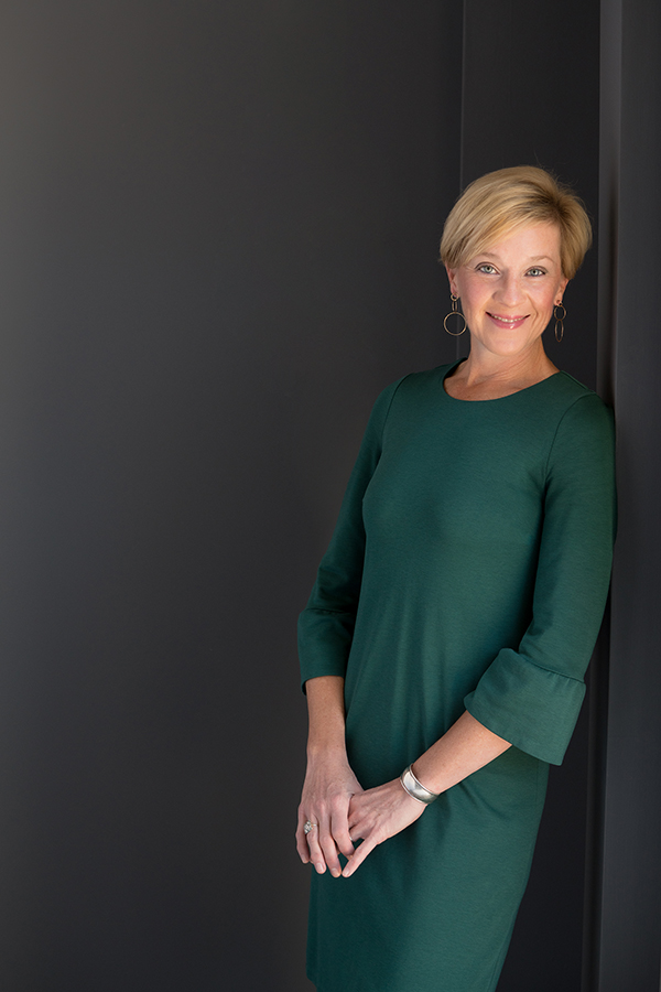 Professional portrait of a person in a green dress standing against a dark wall.