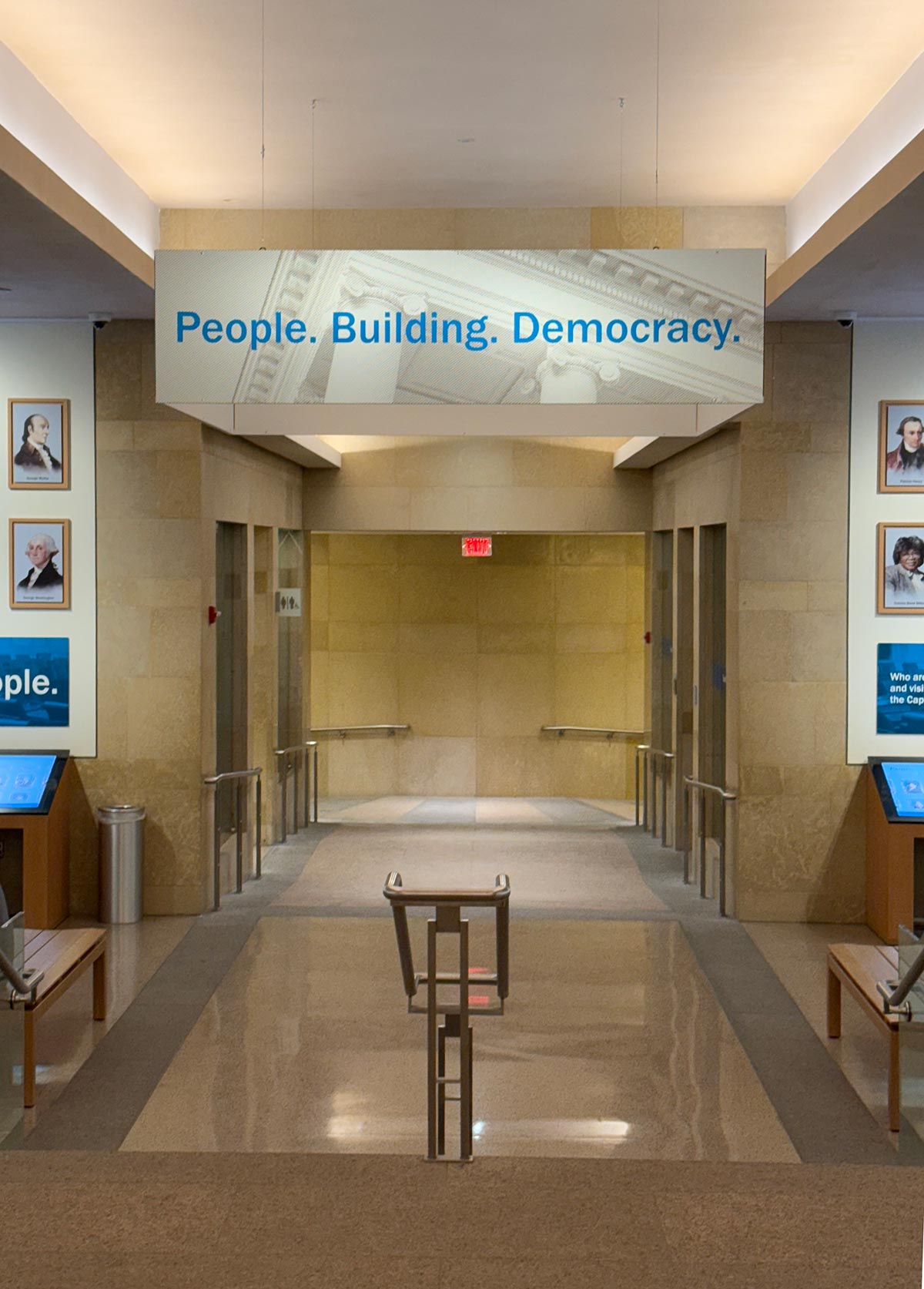 A lobby featuring benches and a sign reading "People Building Democracy" prominently displayed on the wall.